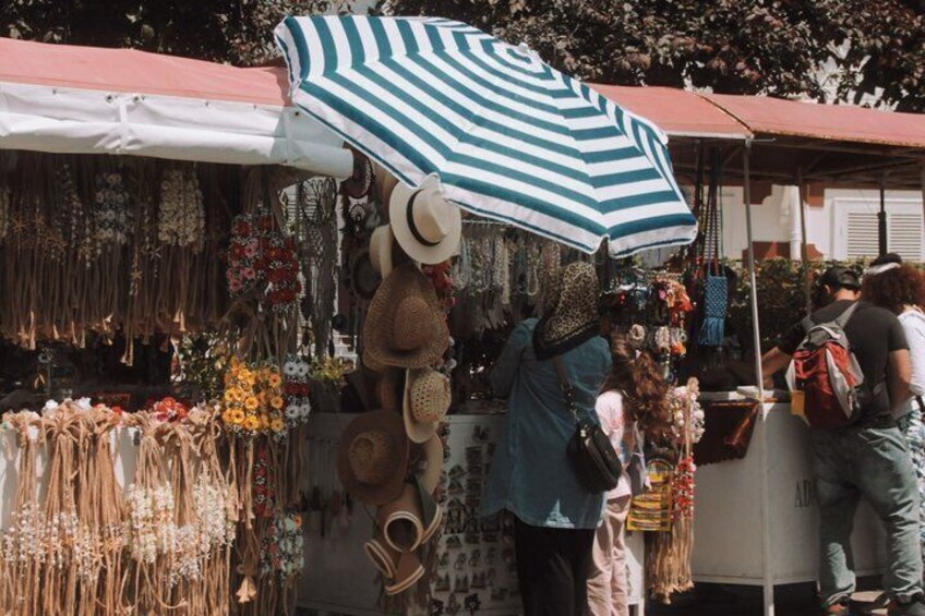 A street market with various stalls selling hats, jewelry, and flowers. 4