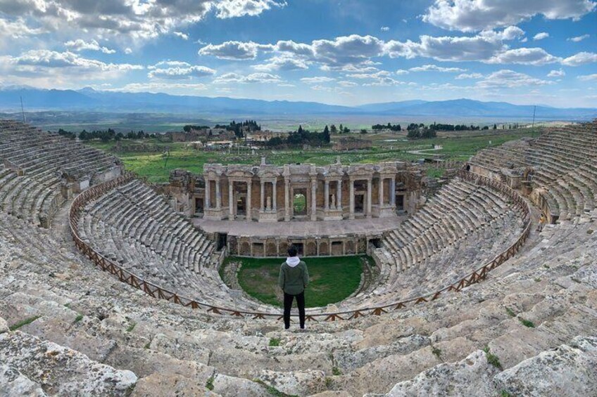 An ancient amphitheater with a central stage and audience seating. 2