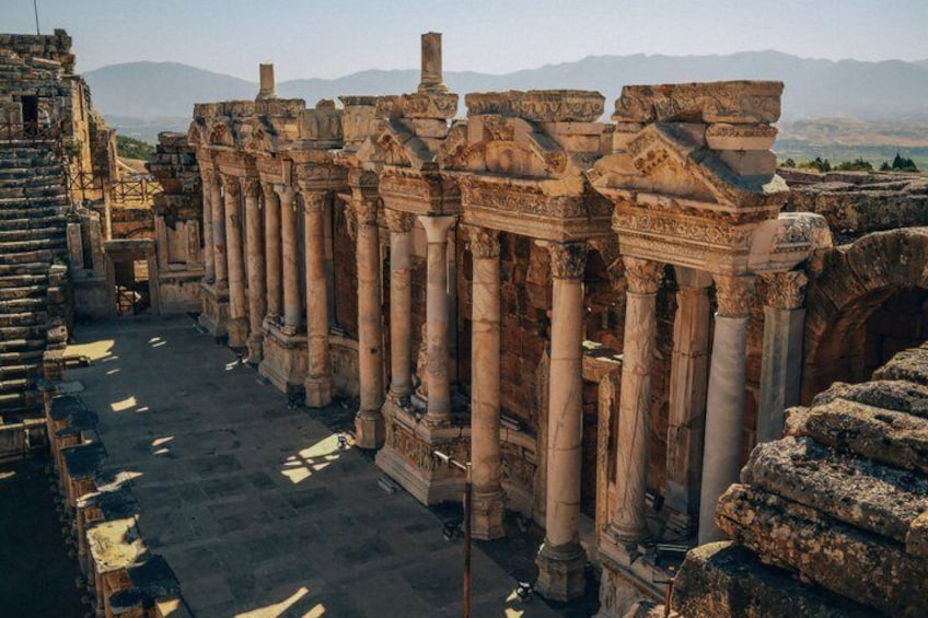 Ancient ruins with columns and arches, set against a mountainous backdrop. 1