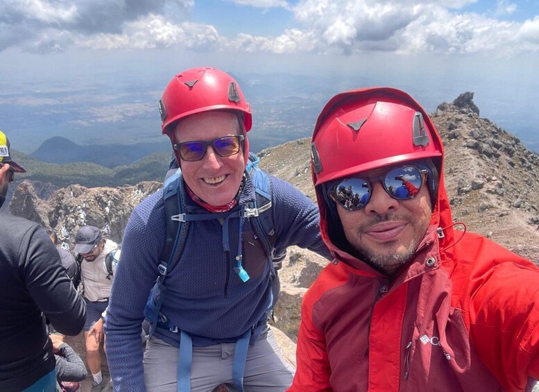 Two people wearing red helmets and hiking gear on a mountain with rocky terrain and a clear sky. 5