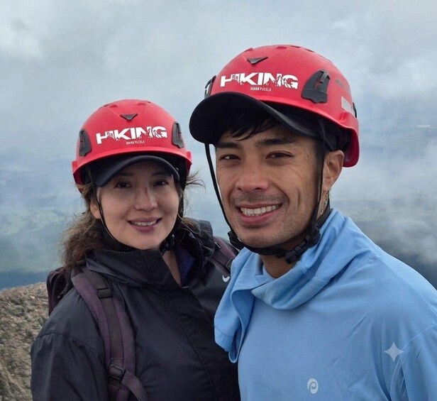 Two people wearing red helmets with the logo 'HIKING' and 'NIKE' on them, standing on a mountain with a cloudy sky in the background. 2