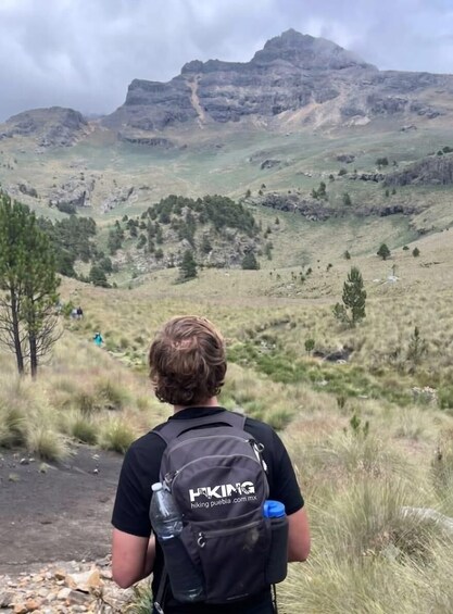 A person hiking with a backpack and a water bottle, overlooking a mountainous landscape with sparse vegetation. 3