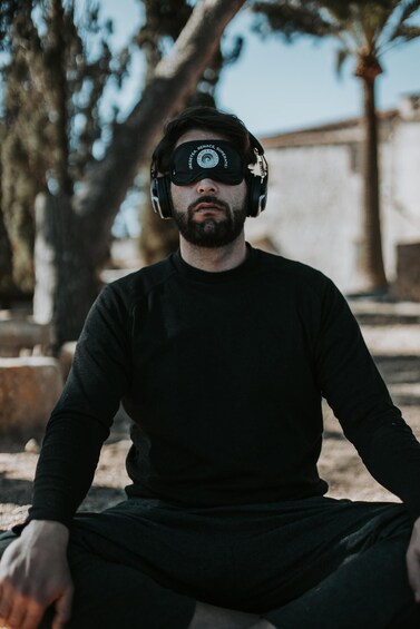 A person sitting outdoors wearing headphones and a dark long-sleeve shirt. 4
