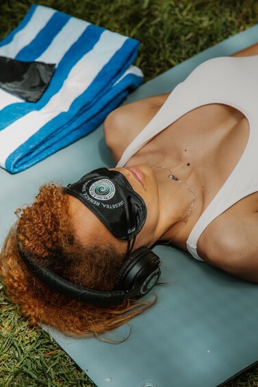 A person lying on a mat with headphones on, surrounded by grass. 3