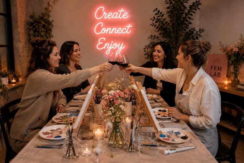A group of people toasting with wine glasses at a table with art supplies and flowers. 1