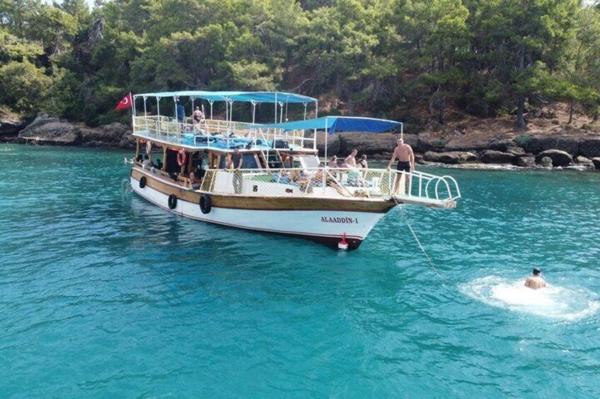A boat with people on board, surrounded by clear blue water and a rocky shoreline with trees. 4