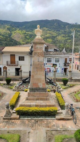 A historical monument with inscriptions, surrounded by a well-maintained garden and a bicycle parked nearby. 5
