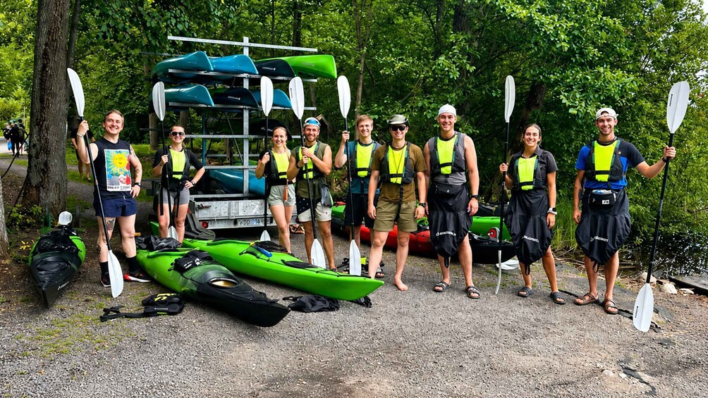 A group of people with kayaks and paddles, standing in a forested area. 3