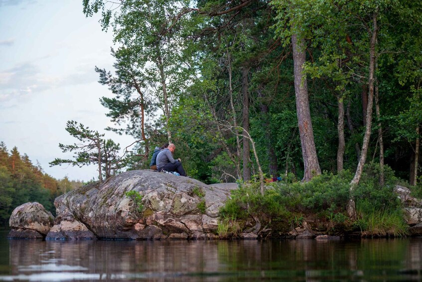A person sitting on a large rock by a calm lake surrounded by dense forest. 2