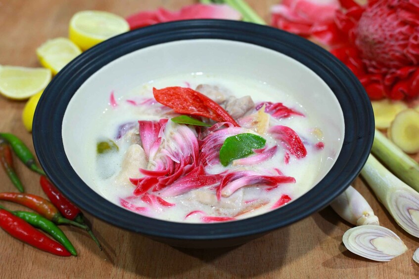 A bowl of creamy soup with red and white vegetables, surrounded by sliced onions, lemon, and chili peppers. 3