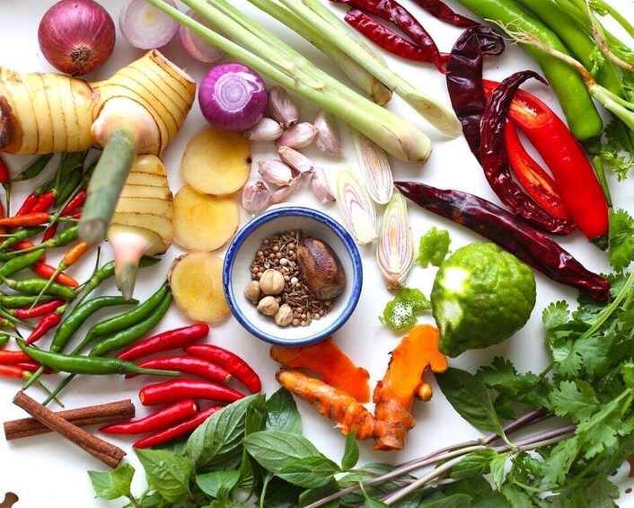 A variety of fresh herbs and spices, including red chili peppers, ginger, garlic, and cilantro, arranged on a white surface. 5