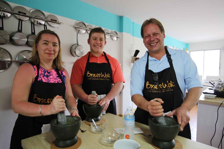 Three people wearing aprons labeled 'Brasstuck' engaged in cooking activities with mortar and pestle. 2