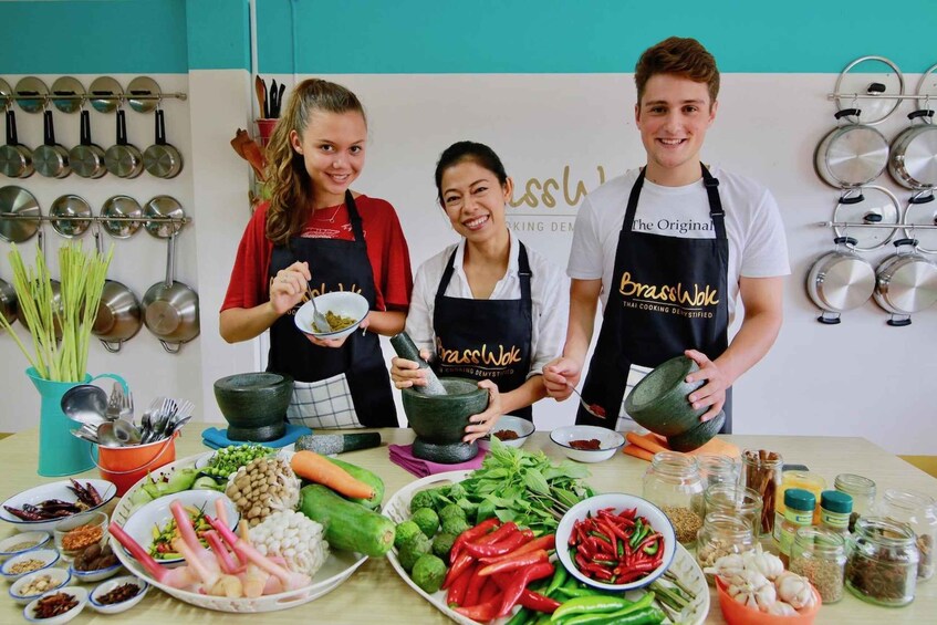 Three people in aprons with cooking utensils and ingredients on a table. 1