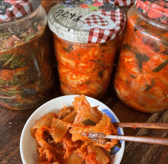 Three jars of kimchi with a bowl of kimchi in the foreground. 3