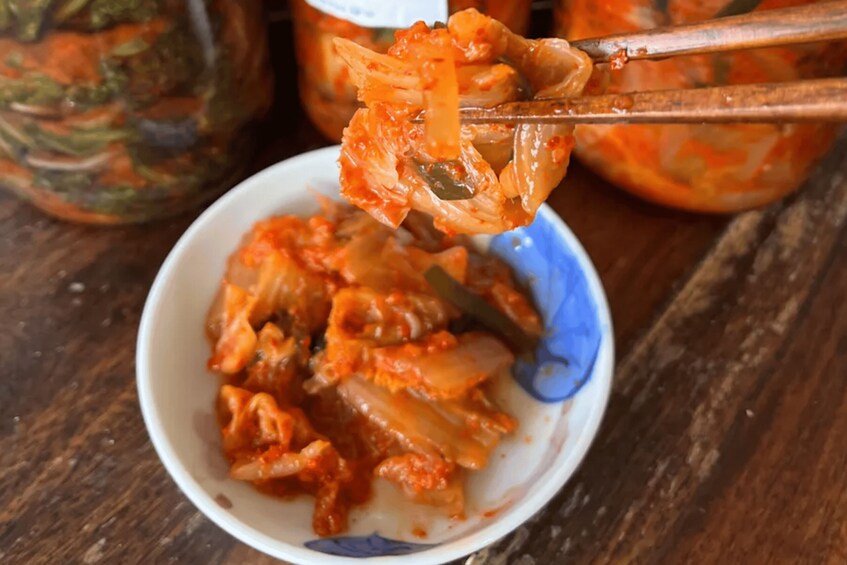 A bowl of kimchi with chopsticks lifting a piece. 1