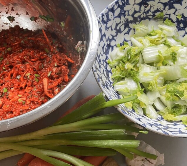 A metal bowl with a red mixture, a bowl of chopped green vegetables, and raw green onions. 2