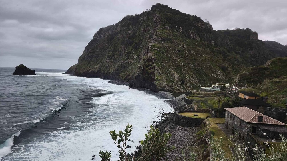 A rugged coastline with a large rock formation, a beach with waves, and a small settlement with traditional buildings. 3
