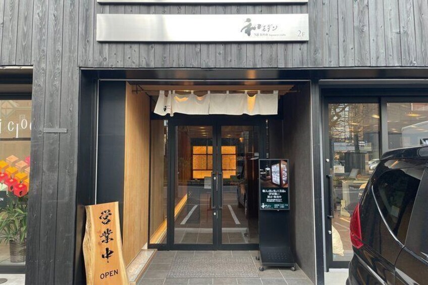 A wooden building entrance with a sign, a bag with Japanese characters, and a car parked outside. 3