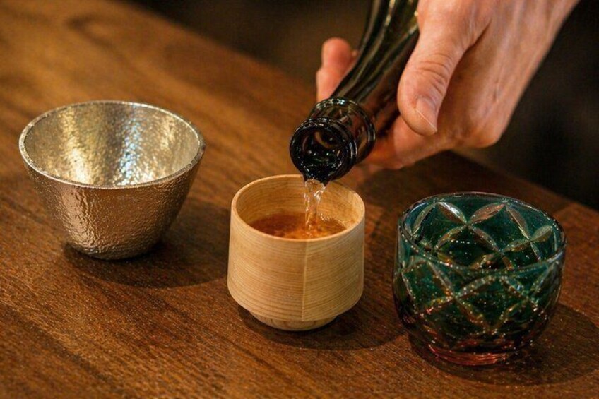 A hand pouring a liquid from a bottle into a wooden cup. 1