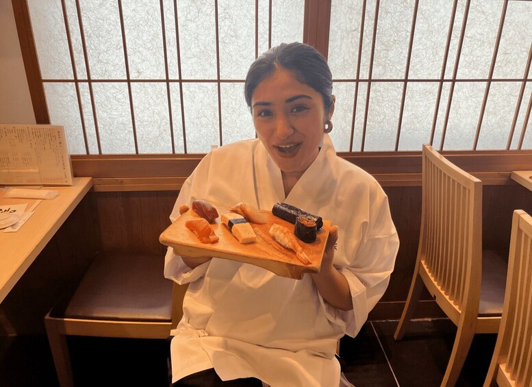 A person seated at a wooden table in a restaurant, holding a tray with various sushi pieces. 2