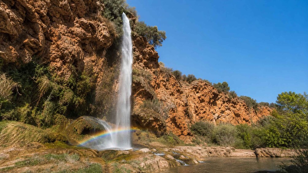 A waterfall with a rainbow, surrounded by rocky cliffs and greenery. 2