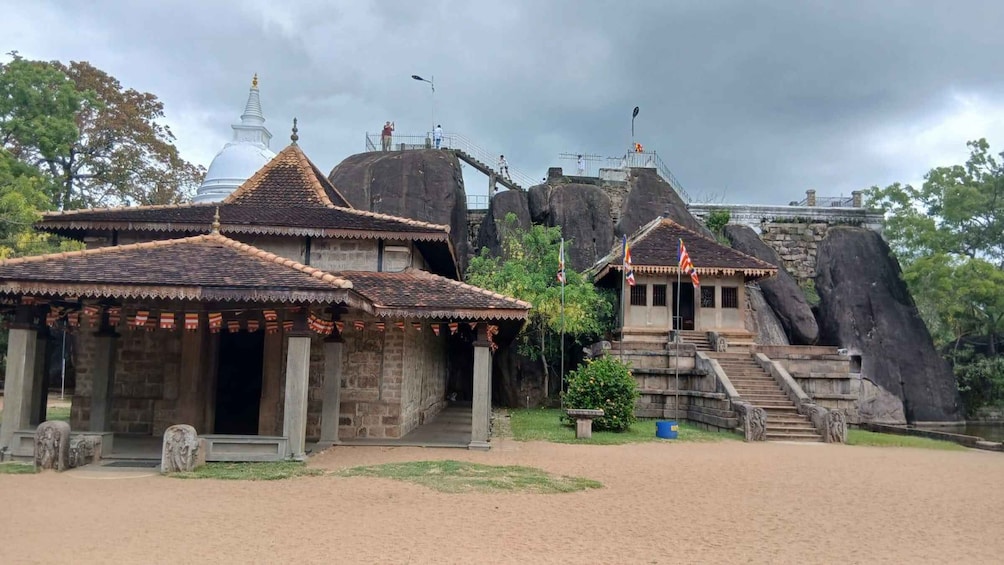 A temple complex with traditional architecture, including a large rock formation and a white stupa. 3