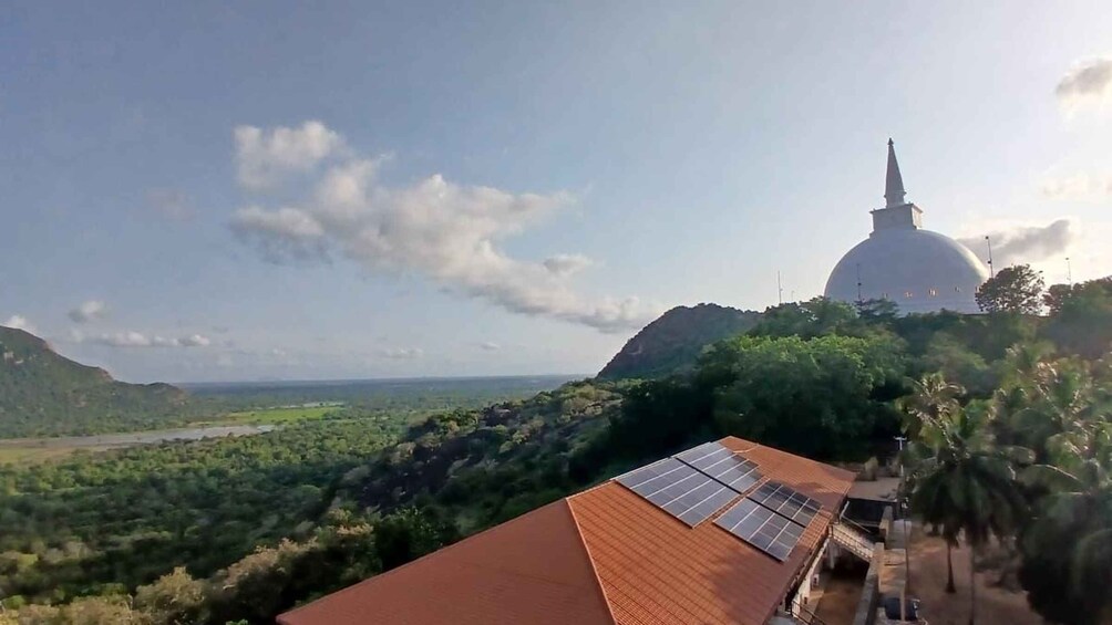 A landscape with a large white dome structure, solar panels on a building, and dense green vegetation. 1