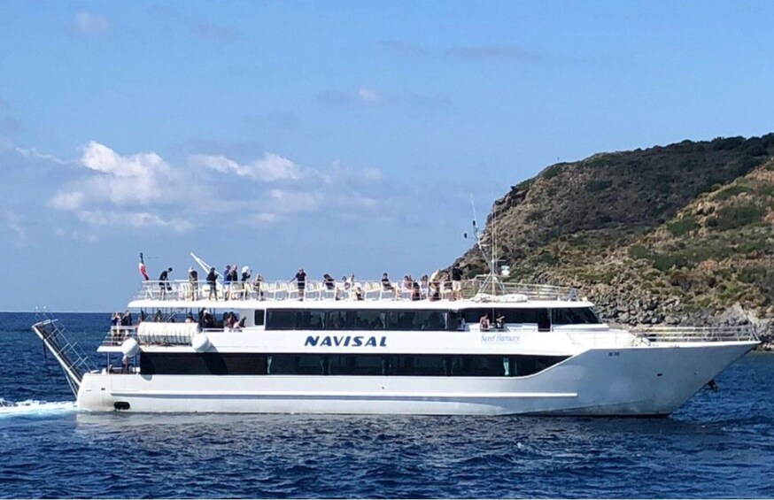 A large white yacht named NAVISAI on the water with passengers on deck, surrounded by a rocky coastline. 3