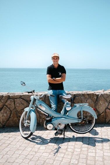 A person standing next to a vintage blue bicycle on a stone wall by the sea. 4