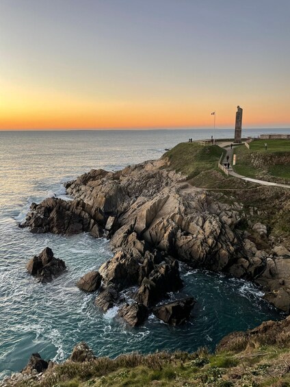 A coastal landscape with rocky cliffs, a grassy path, and a monument. 3