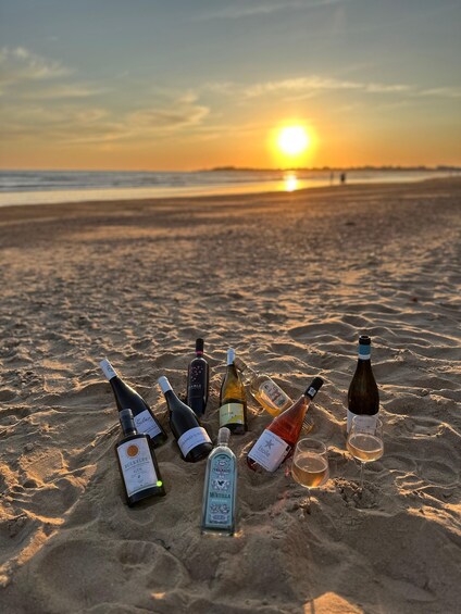 Bottles of alcohol and a glass on a sandy beach with the sun setting in the background. 1