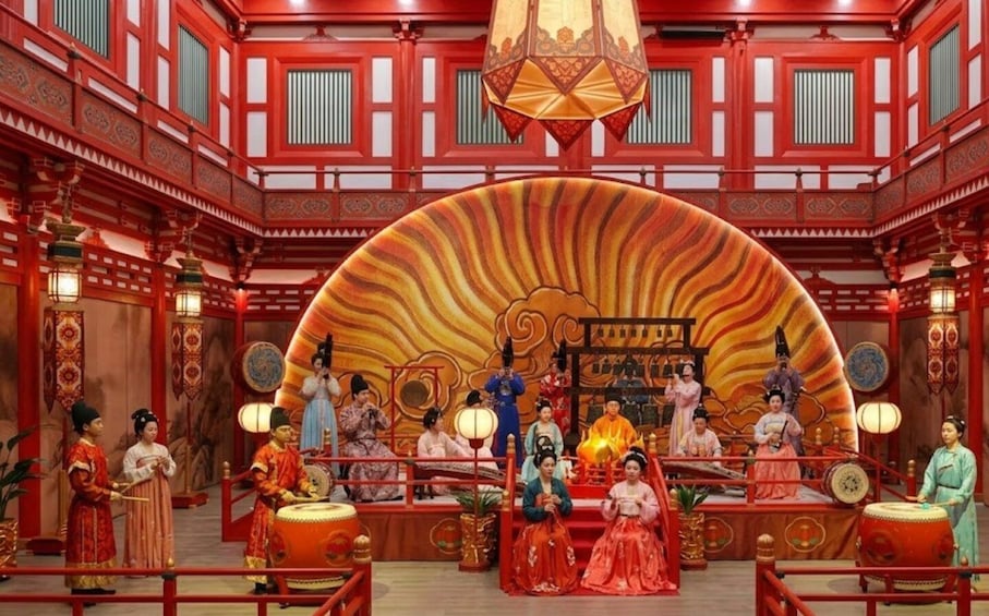 A traditional Chinese opera stage with performers in period costumes, a large ornate backdrop, and red architectural elements. 2