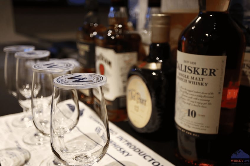A bottle of whisky and several glasses on a bar counter. 1