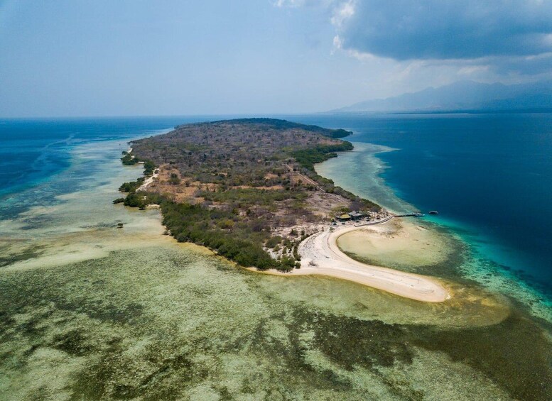 An aerial view of a coastal island with clear waters, a sandy beach, and dense vegetation. 2