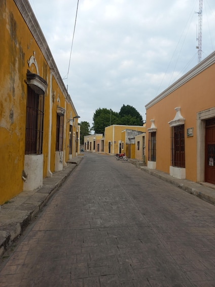 A quiet street lined with yellow buildings, some with barred windows, and a motorcycle parked on the side. 5