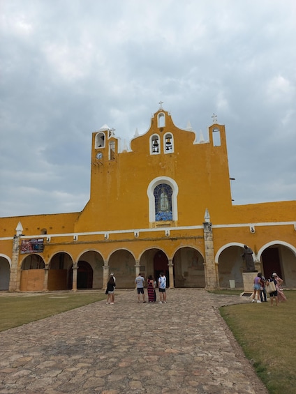 A historic yellow church with a central bell tower, arched walkways, and a mosaic window. 3
