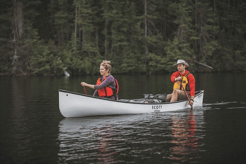 Two people in a canoe on a calm lake surrounded by dense forest. 1