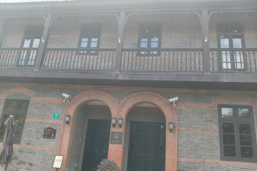 A two-story building with a brick facade, arched entrance, and a balcony with railings. 2