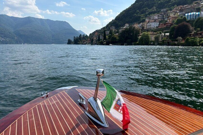A wooden boat on a lake with a flag, mountains, and buildings in the background. 4