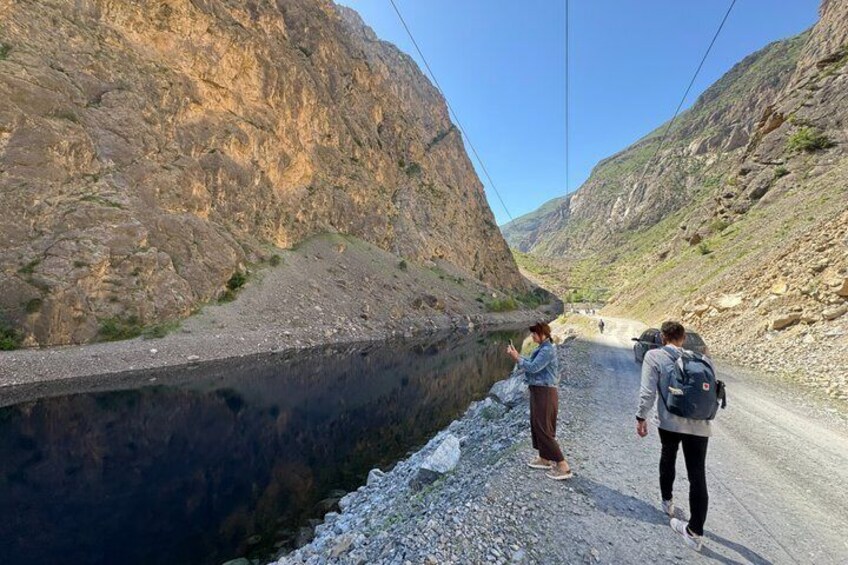 A narrow road flanked by steep rocky cliffs, with two people walking along the roadside. 4