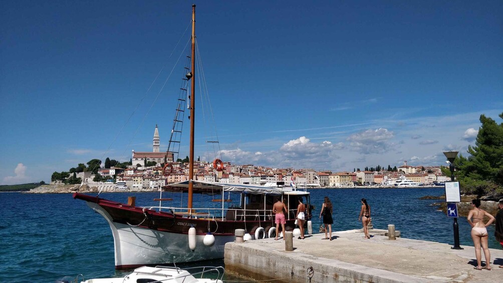 A coastal town with a historic tower, a dock with a sailing boat, and people by the water. 1