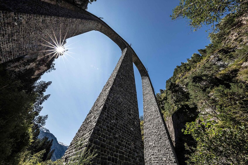 A stone bridge arching over a valley with a clear sky above. 1
