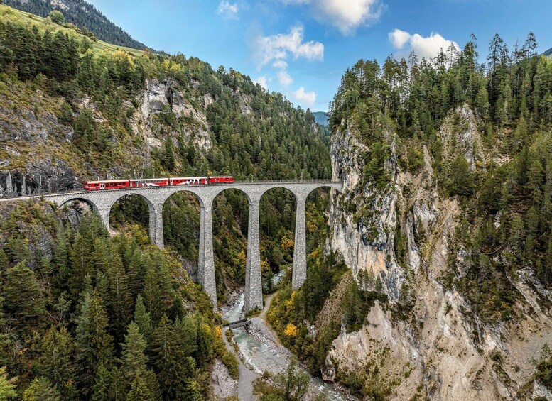 A red train on a stone viaduct through a forested valley. 3