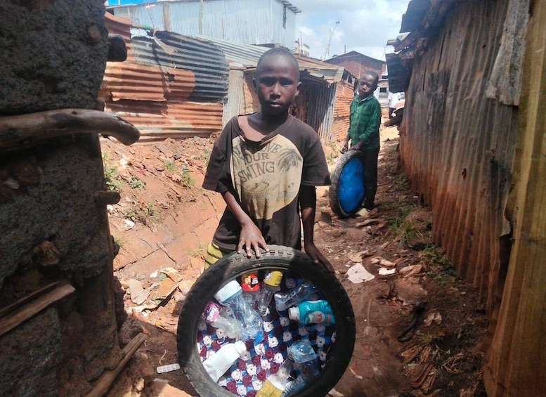 A person holding a large tire filled with plastic bottles in a makeshift settlement. 4