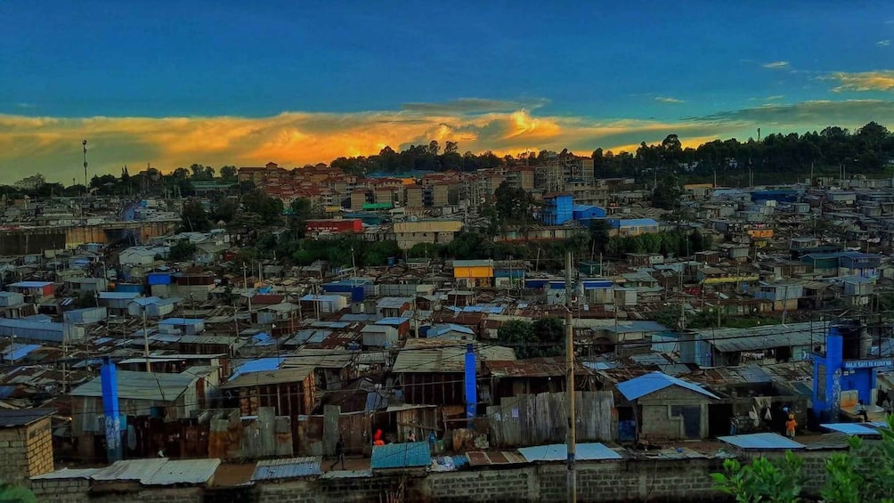 A densely populated urban area with numerous makeshift housing structures and a backdrop of a sunset sky. 1