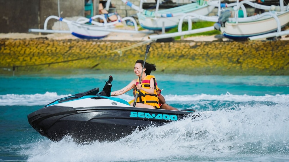 A person riding a Sea-Doo jet ski on a body of water with other boats in the background. 2