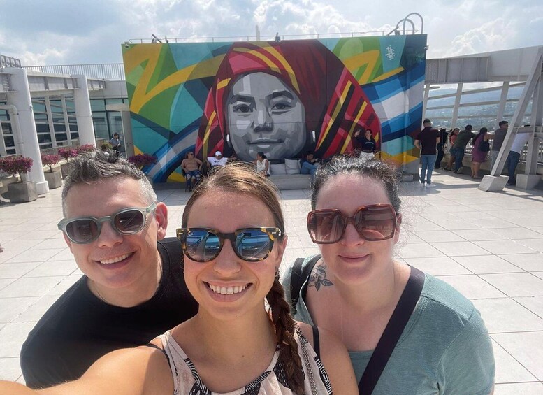 Three people taking a selfie in front of a colorful mural with geometric patterns. 4
