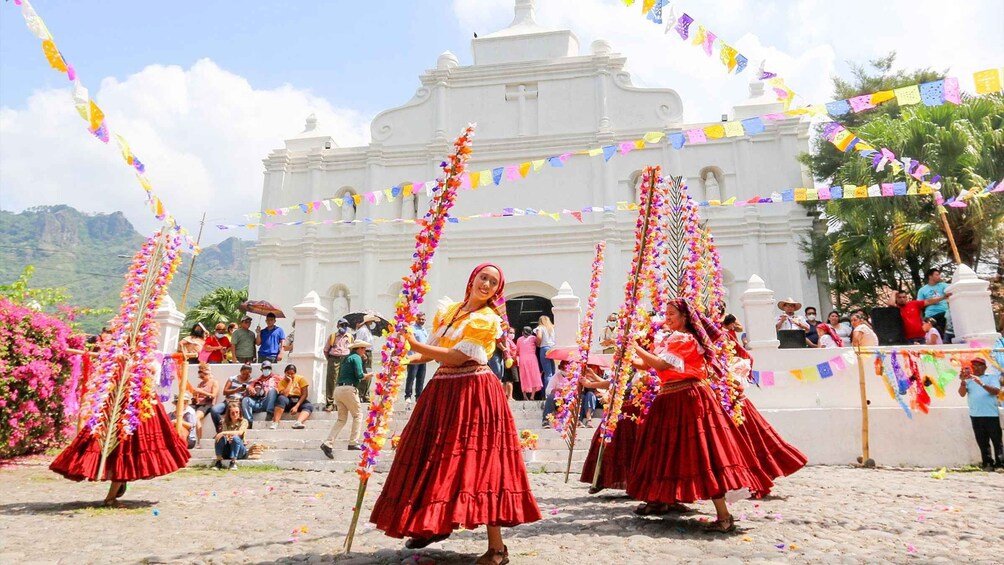 A traditional dance performance in front of a white church with colorful flags. 3