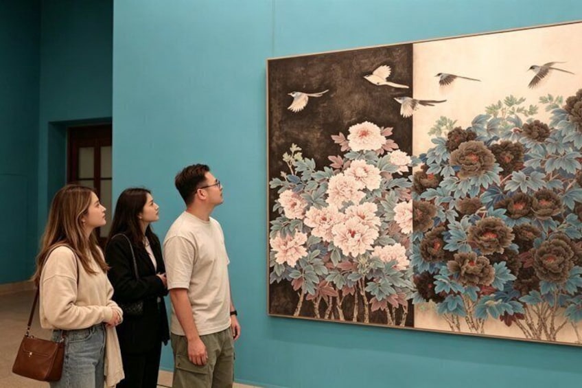 Three people observing a large floral painting with birds in an art gallery. 1