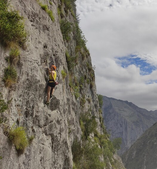A person rock climbing a steep, rocky cliff with sparse vegetation. 4